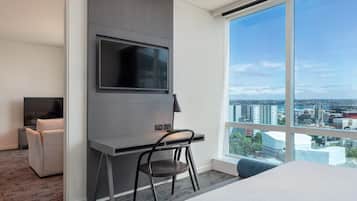 Ein modernes Hotelzimmer mit großem Fenster, einem flachbildfernseher an der Wand, einem Schreibtisch mit Stuhl und einem Bett.