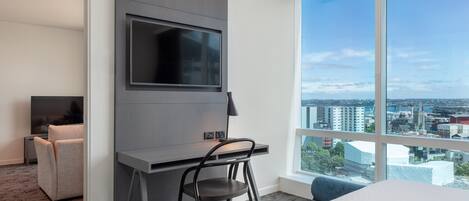 Una habitación de hotel moderna con un ventanal grande, un televisor de pantalla plana en la pared, un escritorio con una silla y una cama.