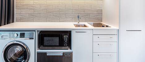 A compact kitchen with a washing machine, microwave, and oven integrated into cabinetry.