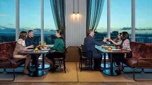 A group of people dining at a table with a city view, in a room with large windows and curtains. - Four Points by Sheraton Auckland (Auckland)