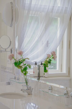 A bathroom with a glass sink, two bottles of liquid soap, and a mirror with a round handle. - Hotel Mignon (Karlovy Vary)