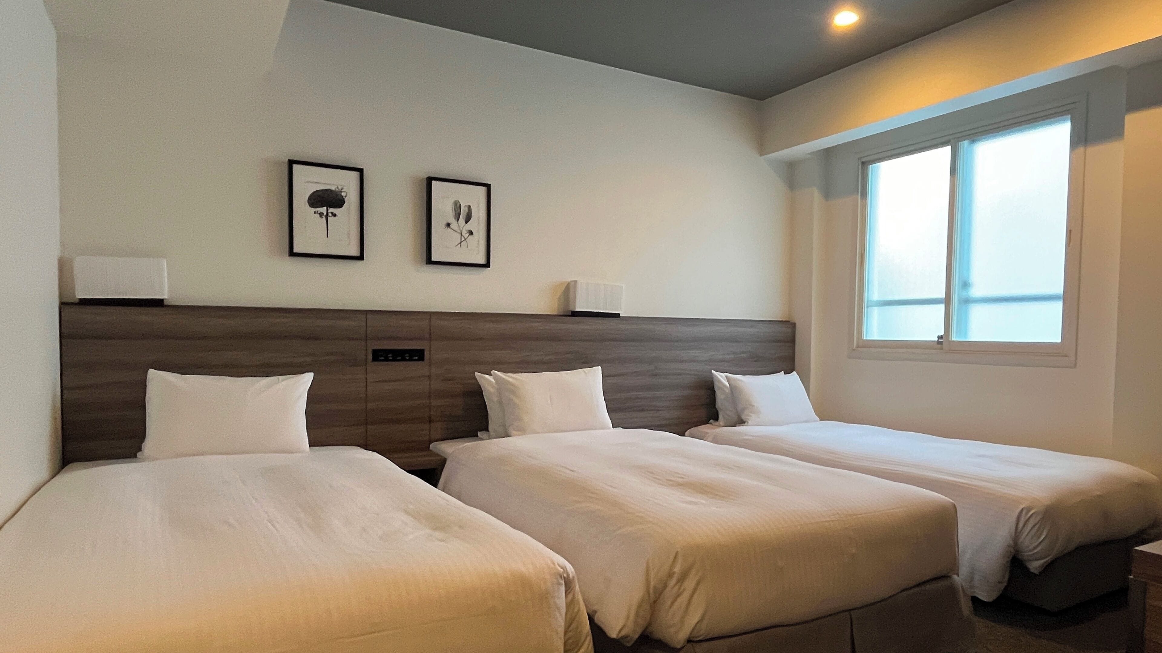 Een hotelkamer met twee eenpersoonsbedden, een houten hoofdbord, nachtlampjes en een raam met uitzicht.