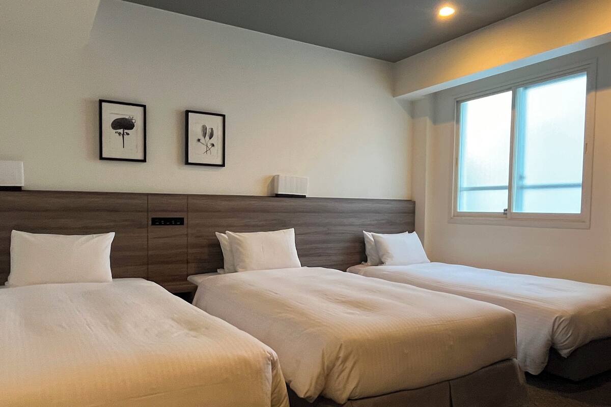 A hotel room with two single beds, a wooden headboard, bedside lamps, and a window with a view.