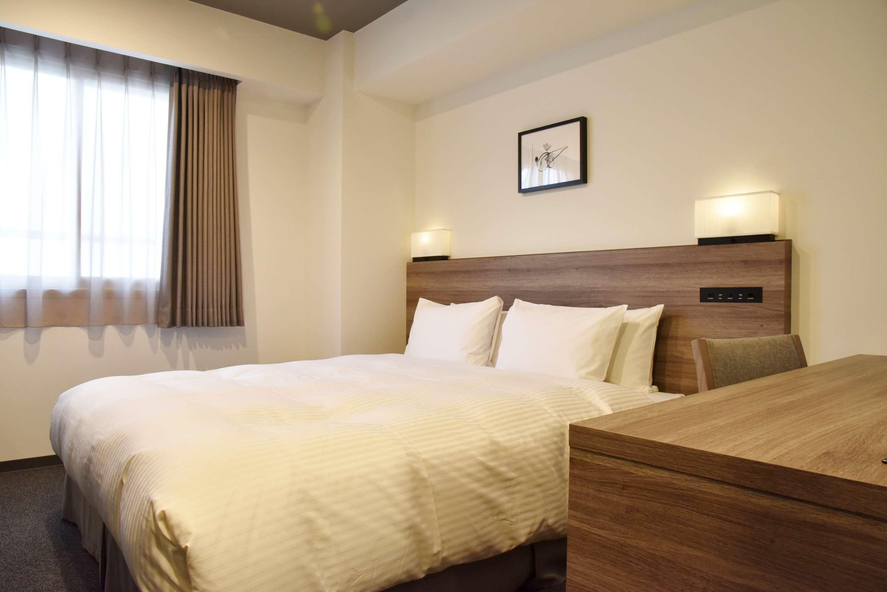 Habitación de hotel con cama, mesitas de noche, escritorio, lámpara y un cuadro en la pared.