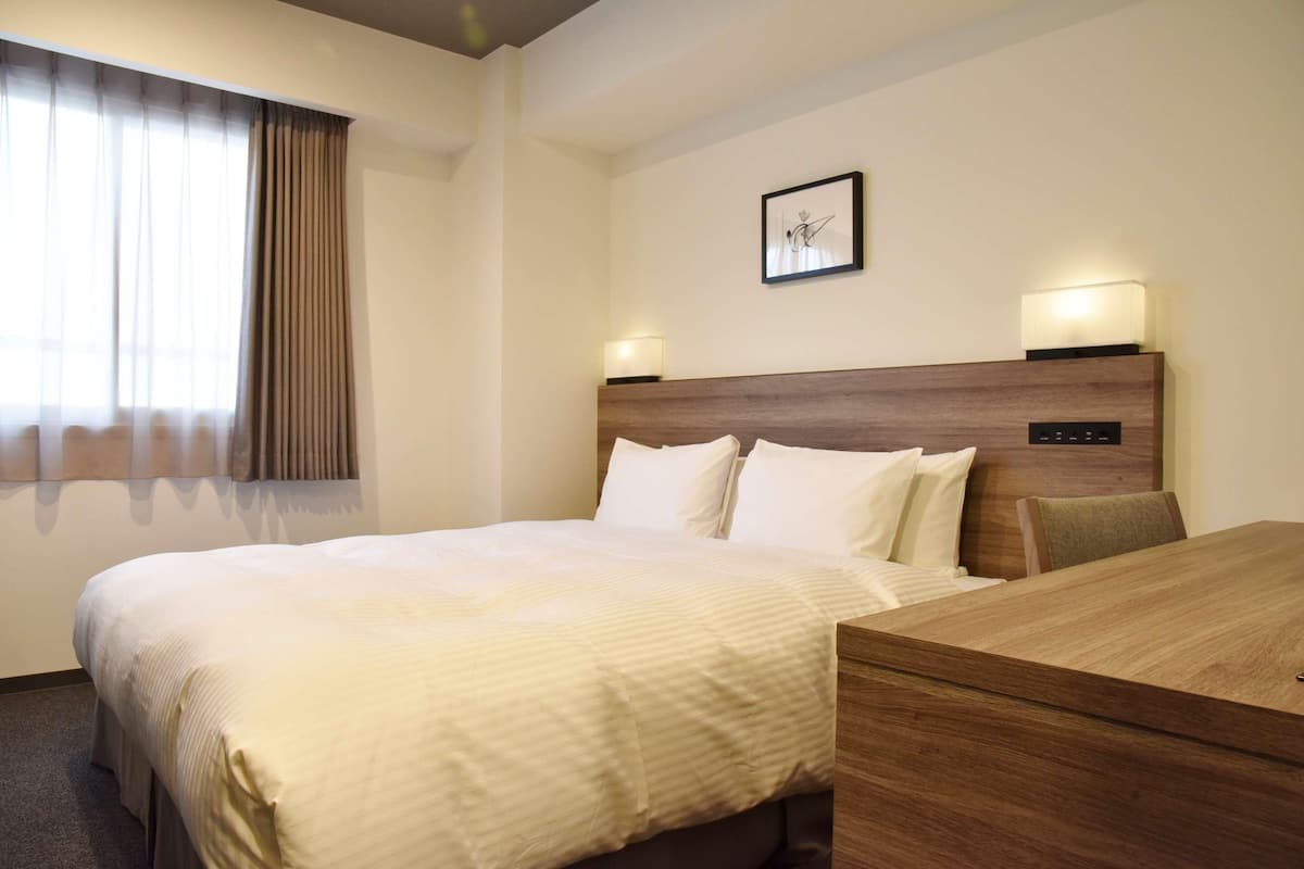 Habitación de hotel con cama, mesitas de noche, escritorio, lámpara y un cuadro en la pared.