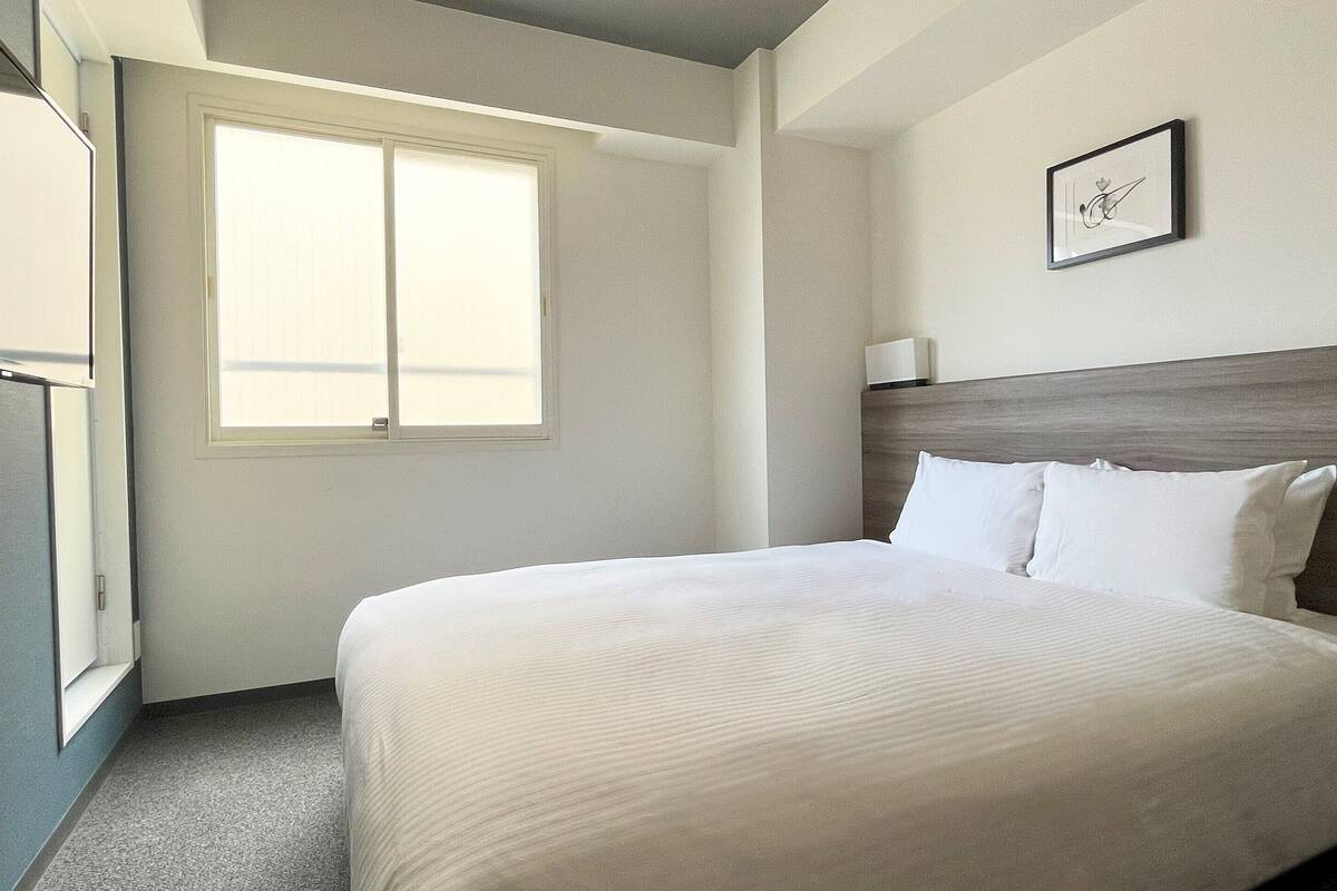 A hotel room with a bed, a window, and a framed picture on the wall.