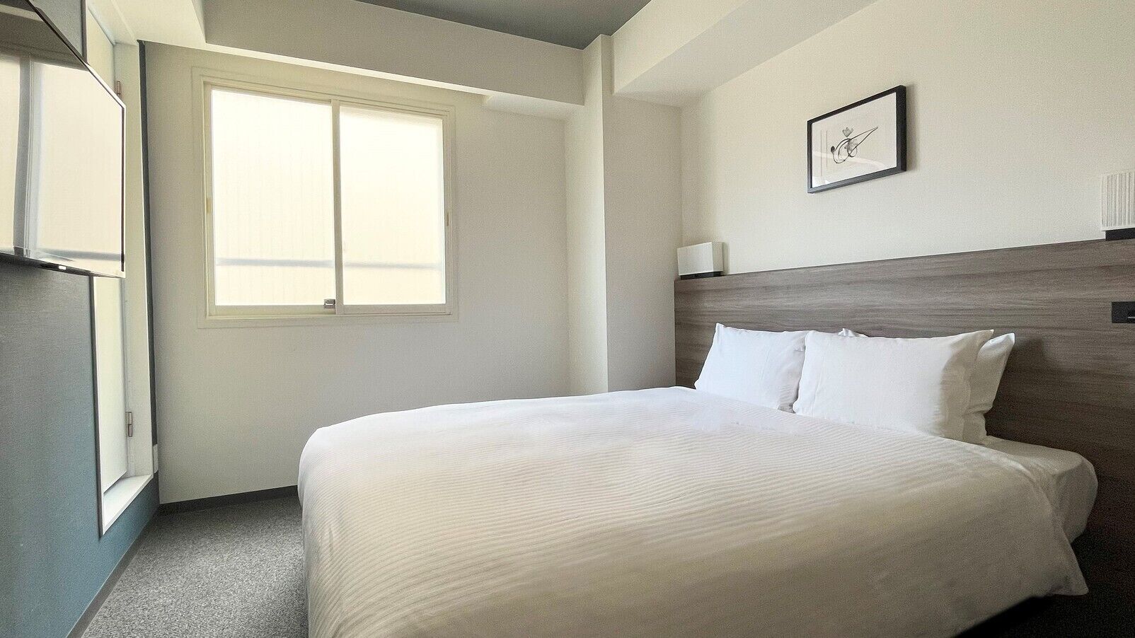 Une chambre d’hôtel avec un lit, une fenêtre, un tableau encadré au mur et un radiateur.