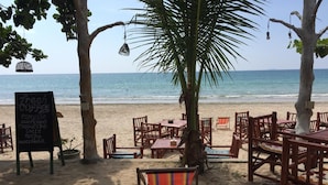 A beachside café with wooden tables and chairs, a chalkboard menu, and a view of the ocean. - Lanta Smile Beach At Klong Dao (Ko Lanta)