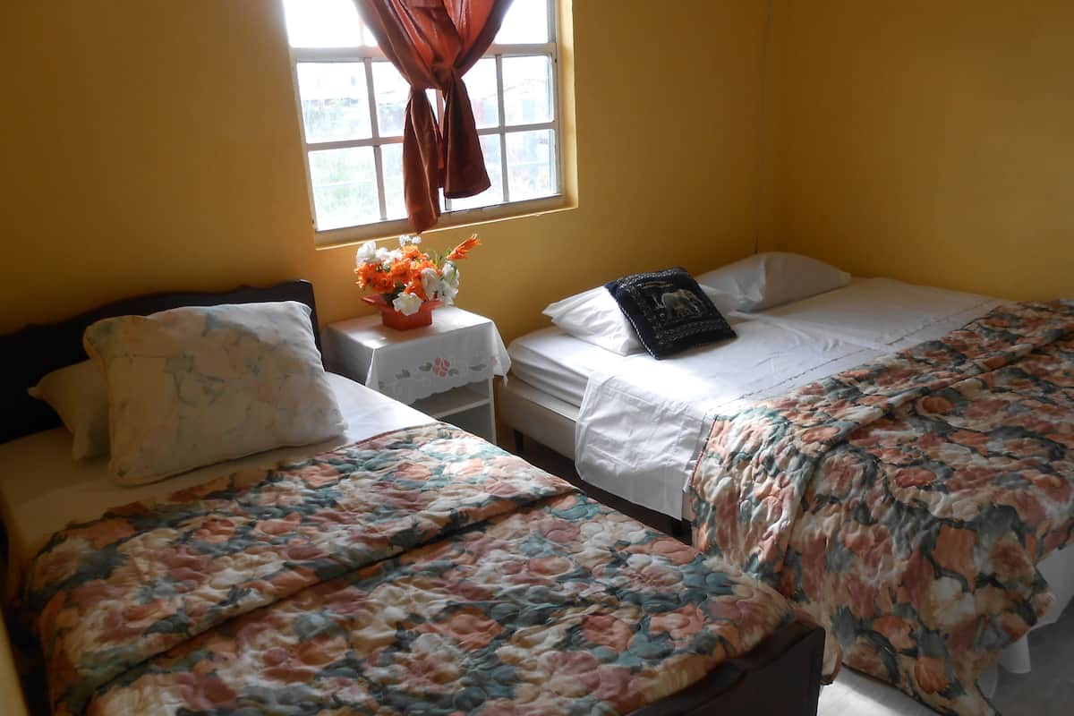 Ein Hotelzimmer mit zwei Betten, einem Nachttisch mit Blumenvase und einem Fenster mit Vorhängen.