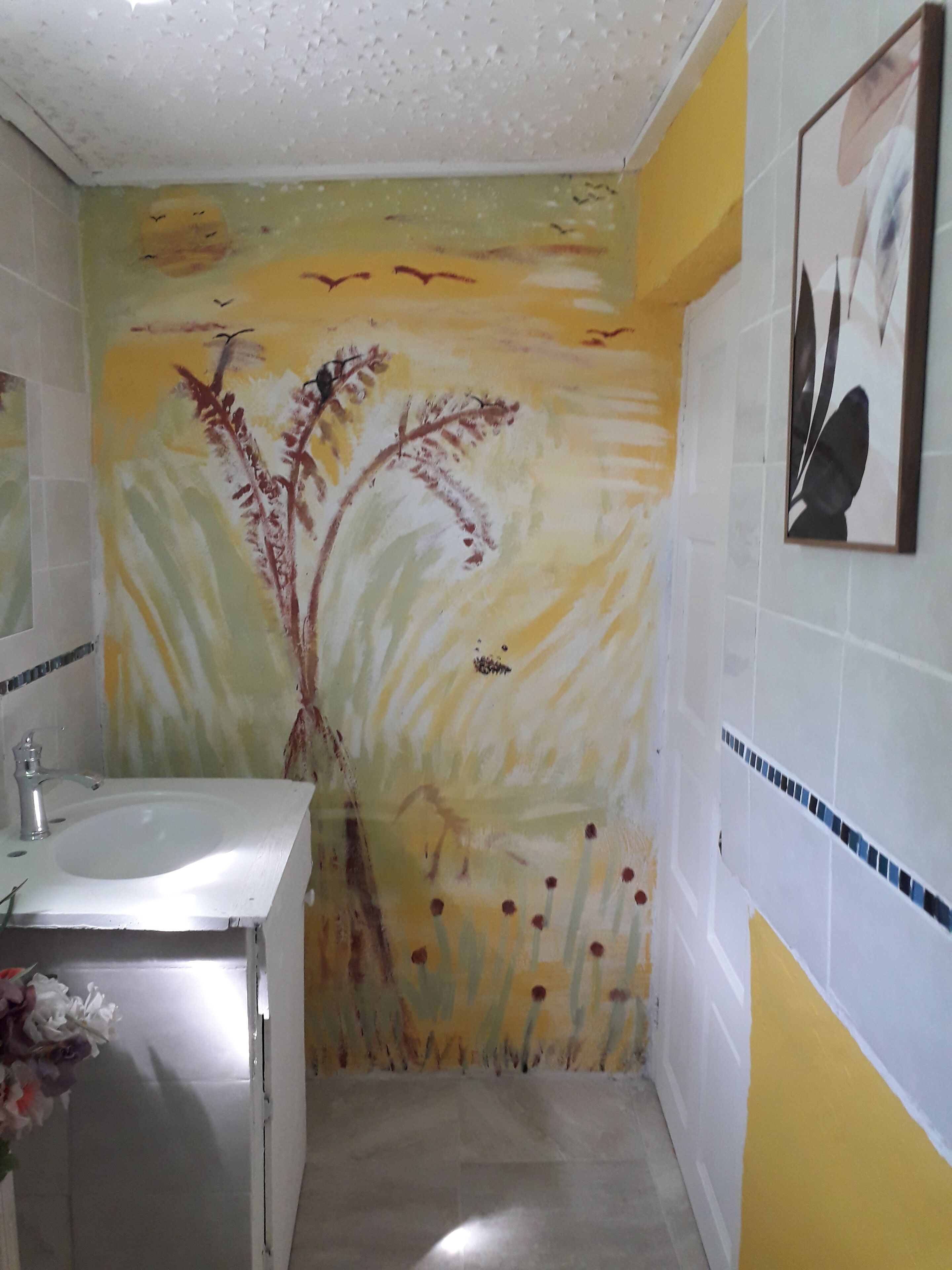 Un baño con lavamanos, espejo y pared con diseño de planta pintada.