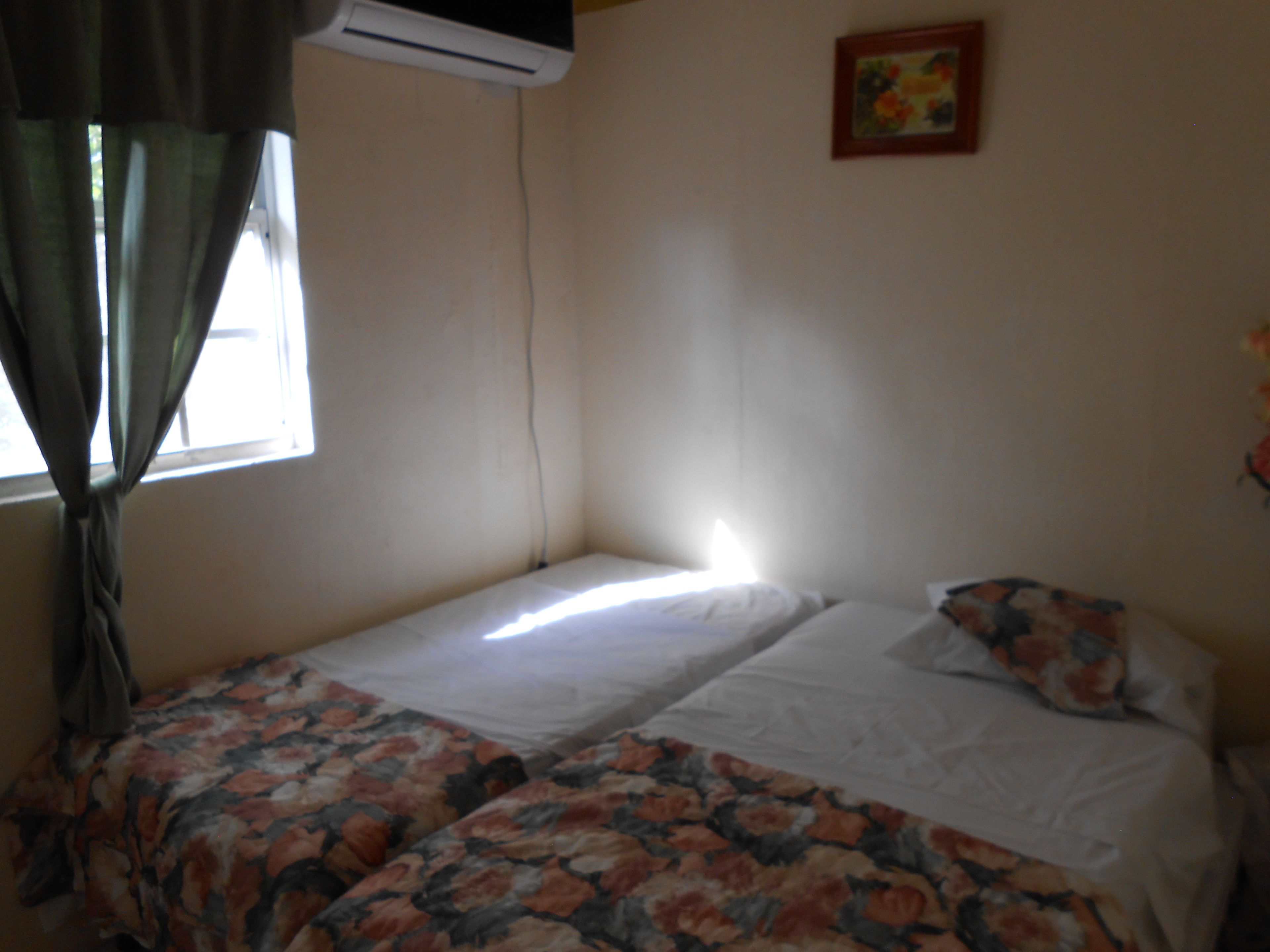Una habitación pequeña con dos camas individuales, una ventana con cortinas y aire acondicionado instalado en la pared.