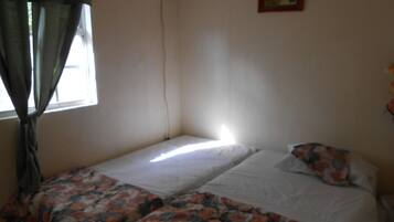 Una habitación pequeña con dos camas individuales, una ventana con cortinas y aire acondicionado instalado en la pared.