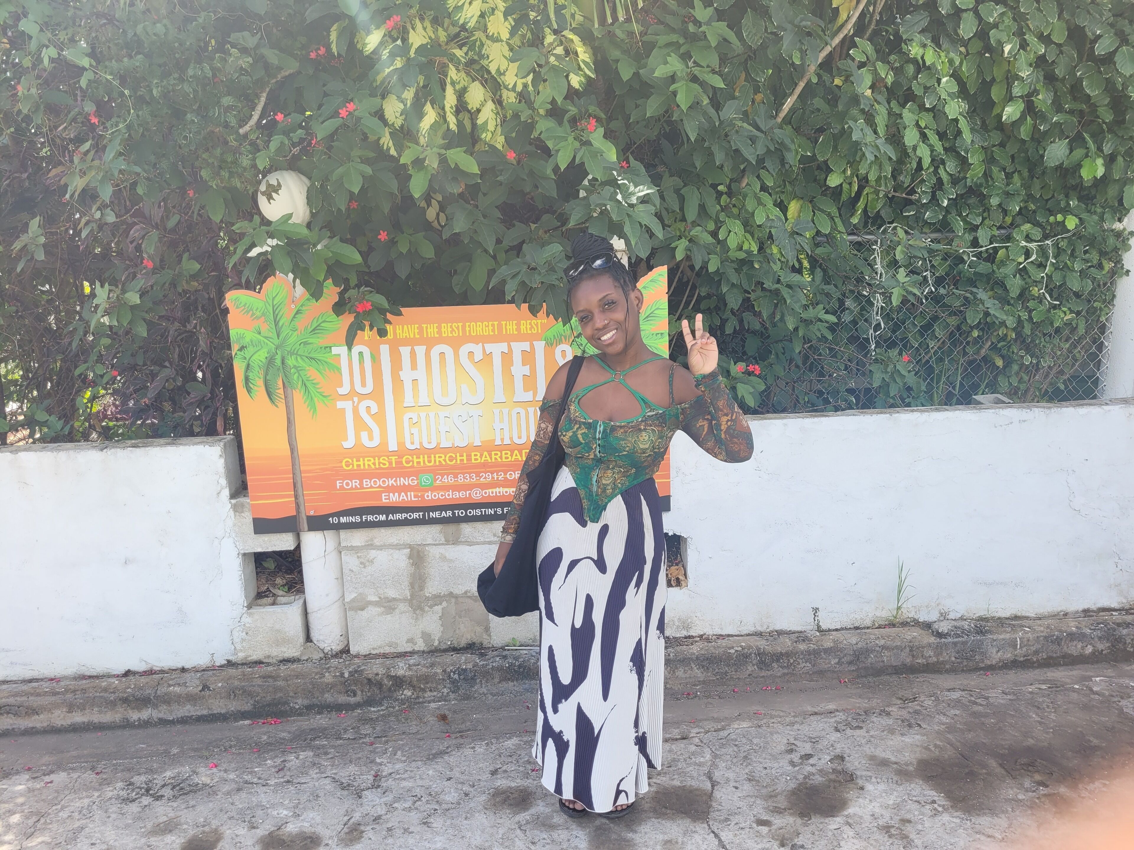 A woman standing in front of a hostel sign with palm trees and a sunset background.