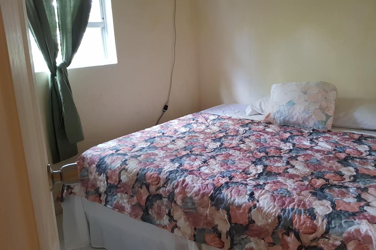 Ein Schlafzimmer mit einem blumigen Bettüberwurf, einem weißen Kissen und einem grünen Vorhang.