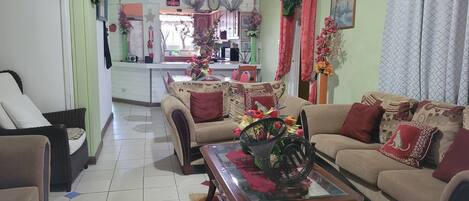 A living room with a sofa, chairs, a coffee table with a vase, and a dining area in the background.