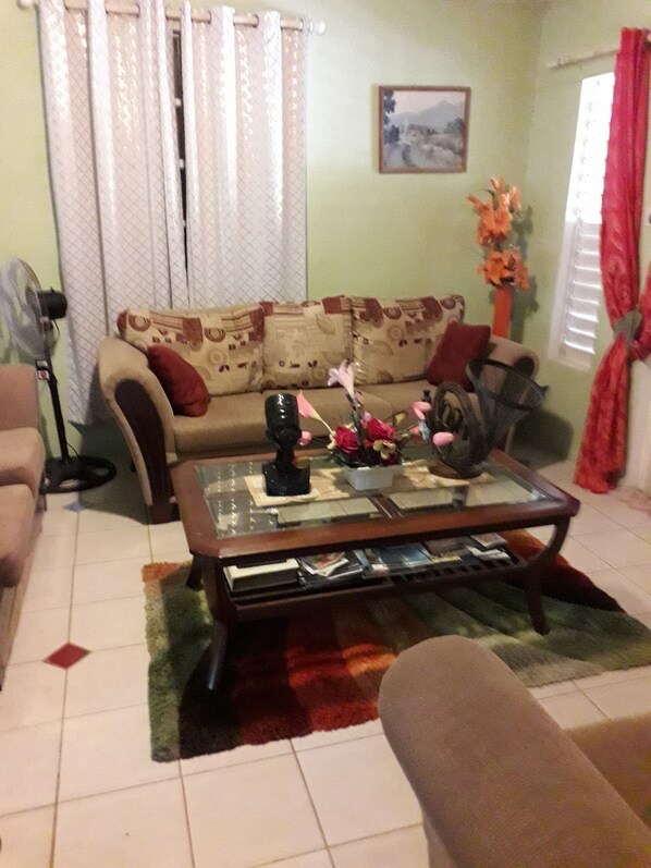 Un salon avec un canapé, une table basse, un ventilateur et un vase rempli de fleurs.