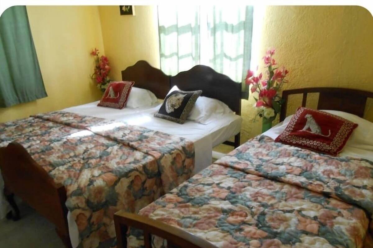 Ein Zimmer mit zwei Betten, jeweils mit floralem Bettbezug und Kissen, einem Holzkopfstück und einem Fenster mit Vorhängen.