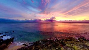 Un paisaje costero con atardecer sobre el océano, costa rocosa y aguas tranquilas.