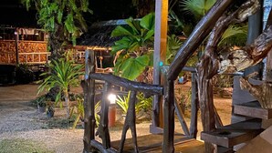 Una escalera de madera con barandilla de metal, rodeada de plantas tropicales y una estructura de techo de paja.