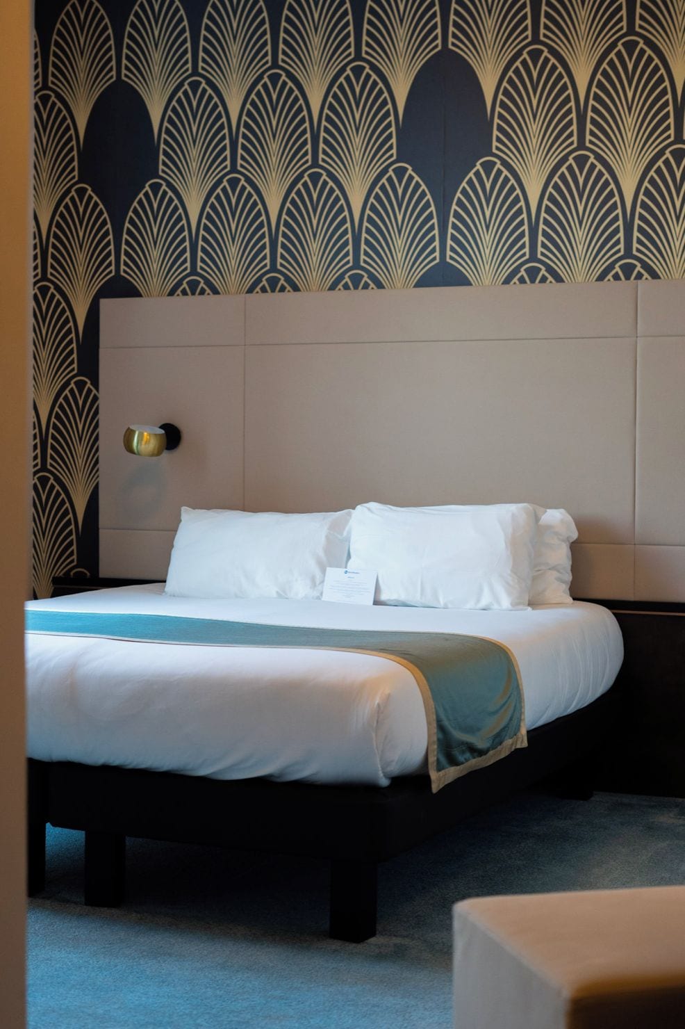 A hotel room with a bed, a nightstand, and a wall with a decorative pattern.