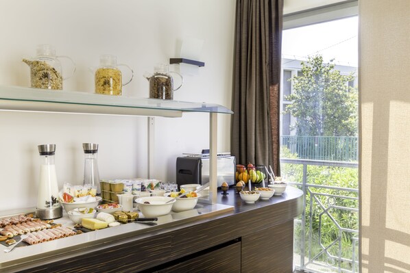 A buffet setup with various food items and beverages on a glass counter, with a view of greenery outside. - Best Western Hotel Journel Antibes-Juan-les-Pins (Antibes)