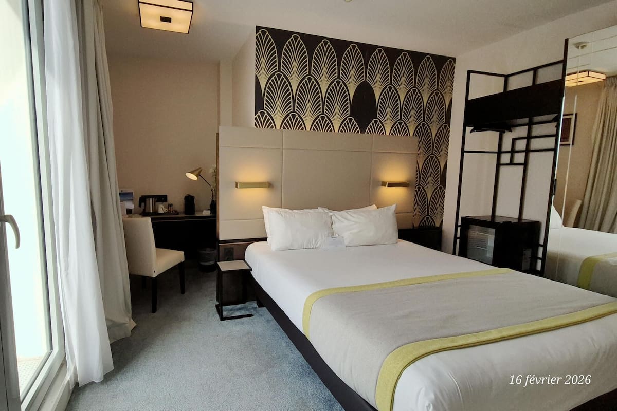 A hotel room with a bed, bedside tables, a desk, a chair, and a window with curtains.