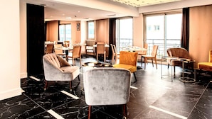 Um hall de hotel moderno com disposição ampla, com vários espaços de estar e grandes janelas com vista para a cidade.