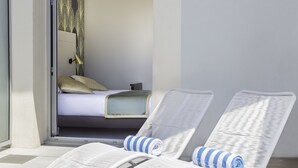 Quarto com cama, janela e duas poltronas de vime brancas com toalhas.