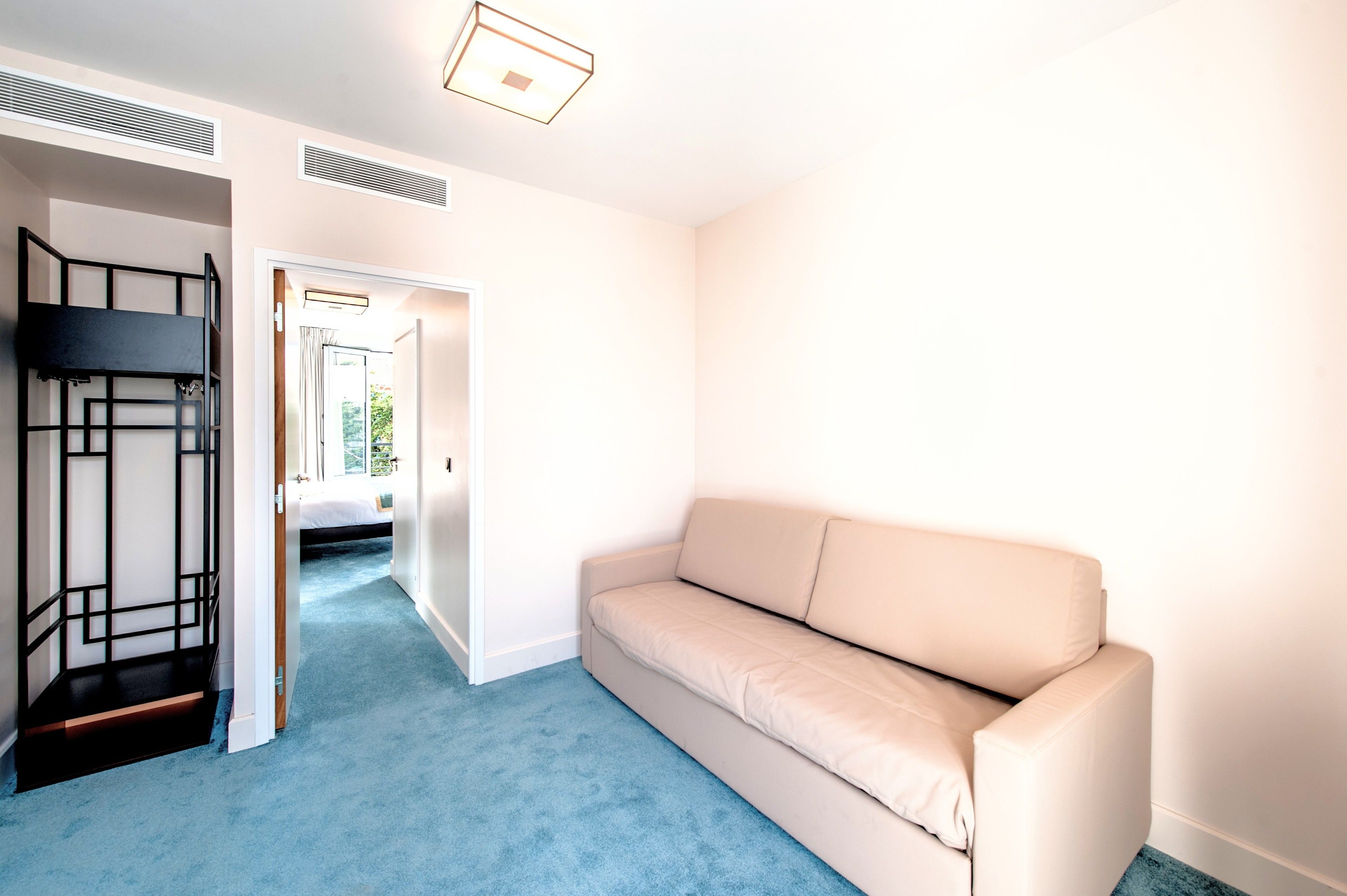 A room with a beige sofa, a bunk bed, and a blue carpet.