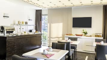 Une chambre d’hôtel moderne dotée d’un coin repas, d’un plan de travail avec un appareil à café et d’un téléviseur à écran plat fixé au mur.