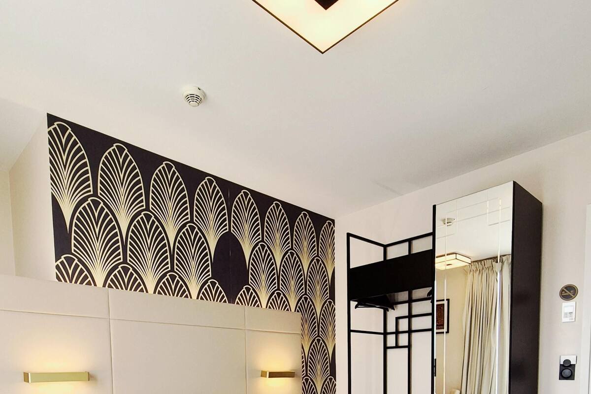 A modern hotel room with a large bed, a decorative wall panel, a mirror, and a ceiling light fixture.