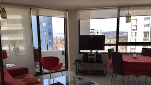 Una sala de estar moderna con una mesa de centro de vidrio, sofás rojos y una zona de comedor con mantel rojo.