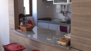 Una cocina moderna con encimera de granito, armarios blancos y un microondas. Se ven dos taburetes rojos en primer plano.