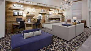 A modern hotel room with a fireplace, a sofa, a desk with a computer, and a patterned carpet. - GrandStay Cannon Falls (Cannon Falls)