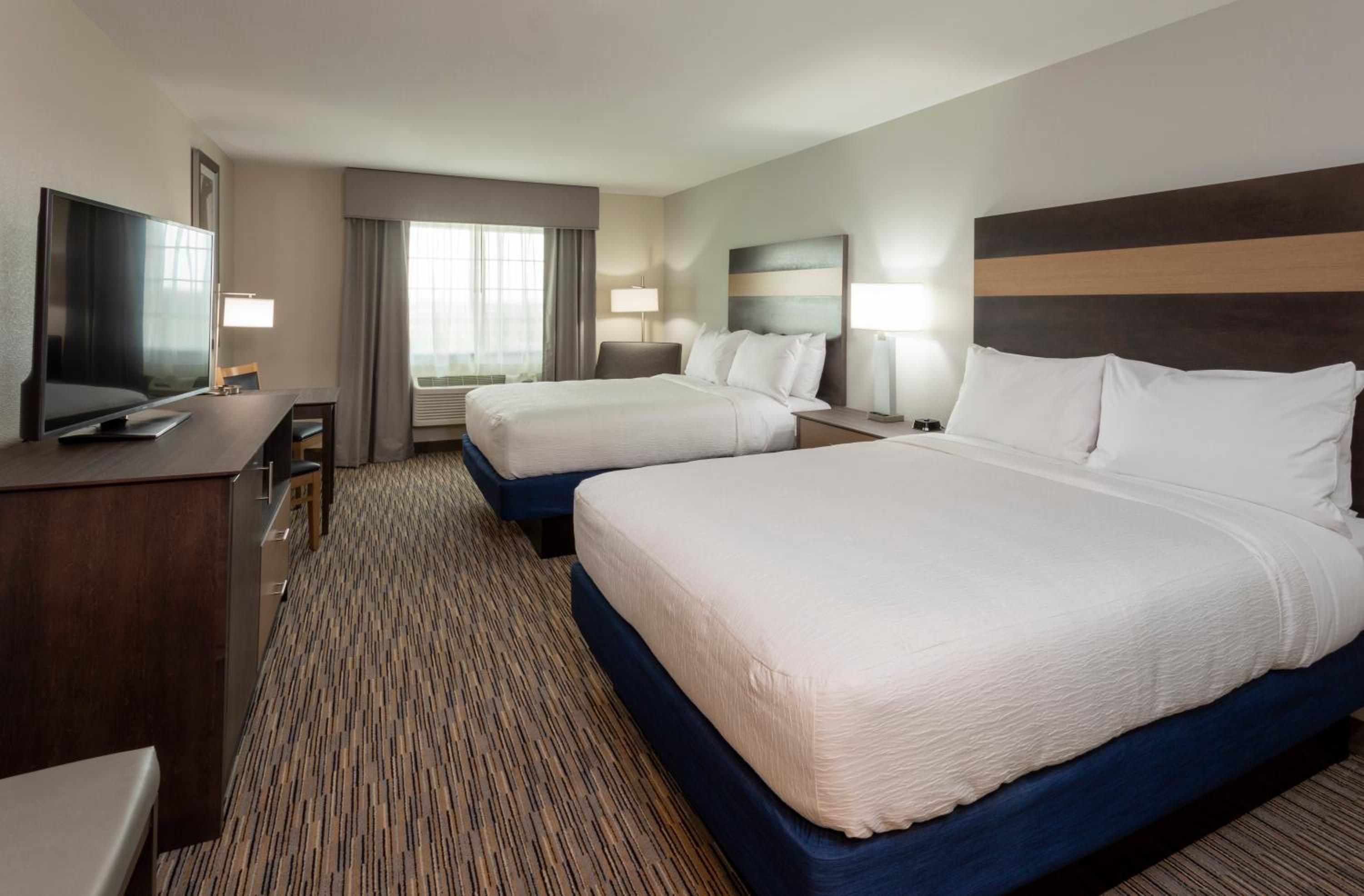 A hotel room with two beds, a desk, a TV, and a window with curtains.