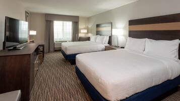 A hotel room with two beds, a desk, a TV, and a window with curtains.