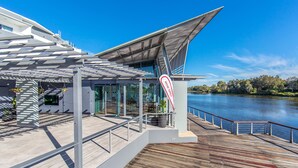 Una terraza moderna al aire libre con piso de madera, barandas de metal y cerramiento de vidrio con vista a un lago.