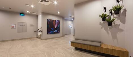 A modern lobby with a marble floor, a digital art display, a fire hose reel sign, and a bench with a wooden bench and a black shelf.