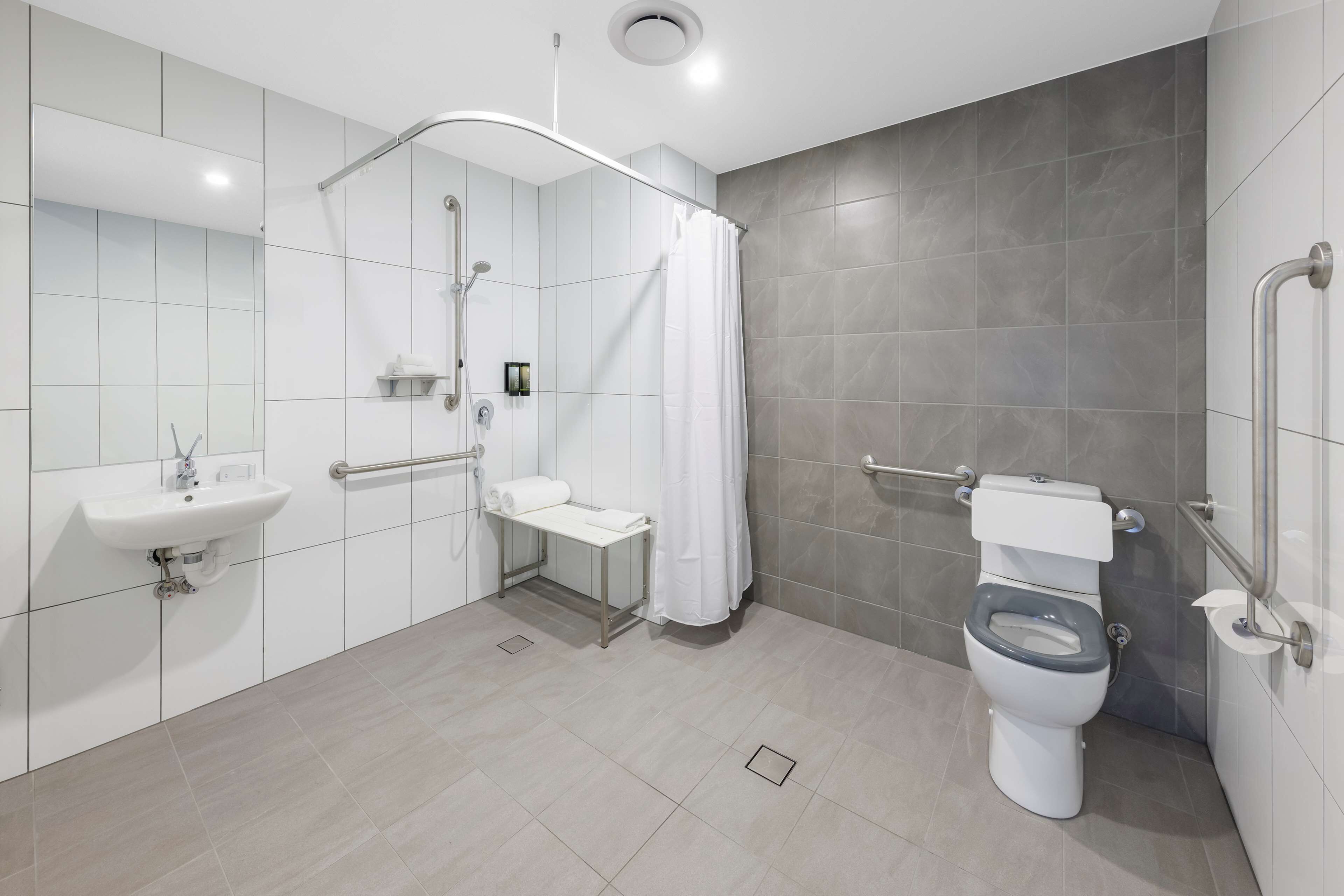 Un baño moderno con ducha, inodoro, lavamanos y barras de apoyo.