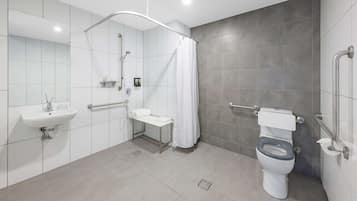 Un baño moderno con ducha, inodoro, lavamanos y barras de apoyo.