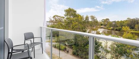 A balcony with two chairs and a table, overlooking a river and greenery.
