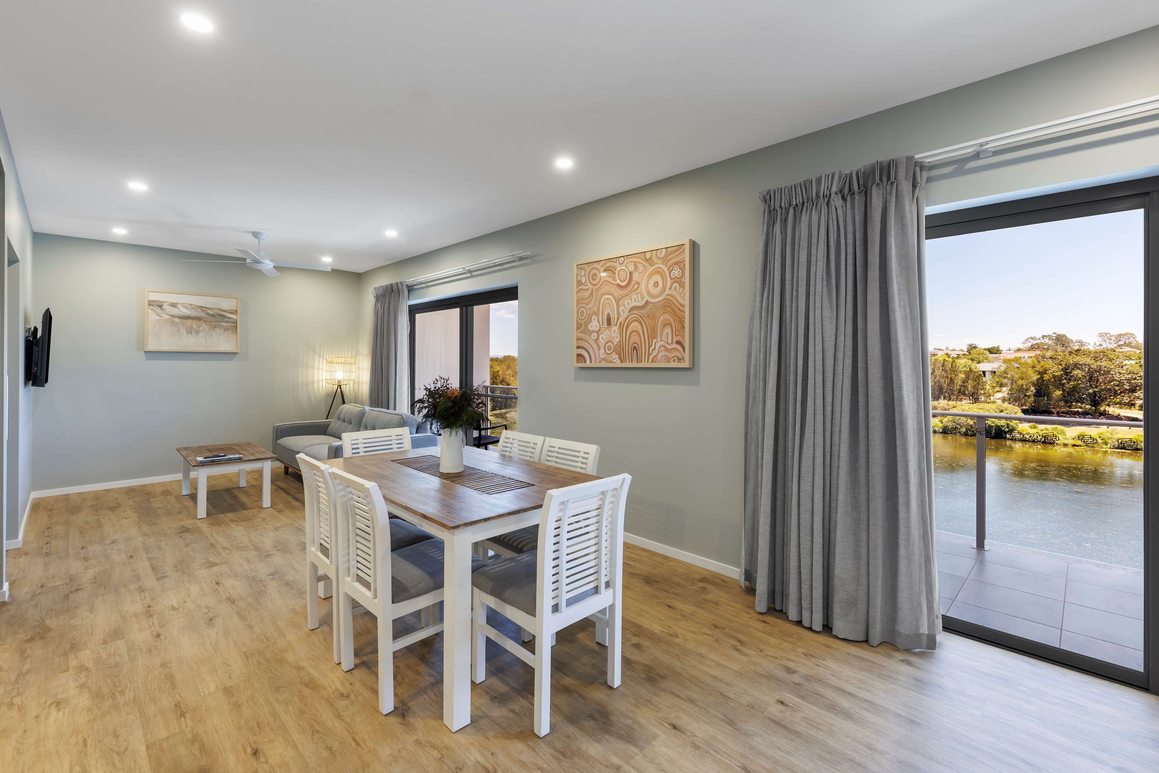 A spacious dining area with a wooden table and white chairs, a ceiling fan, and a view of a garden through a large window.