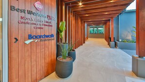 Un pasillo con paneles de madera, plantas en macetas y letreros de Best Western Plus y Restaurante Boardwalk.