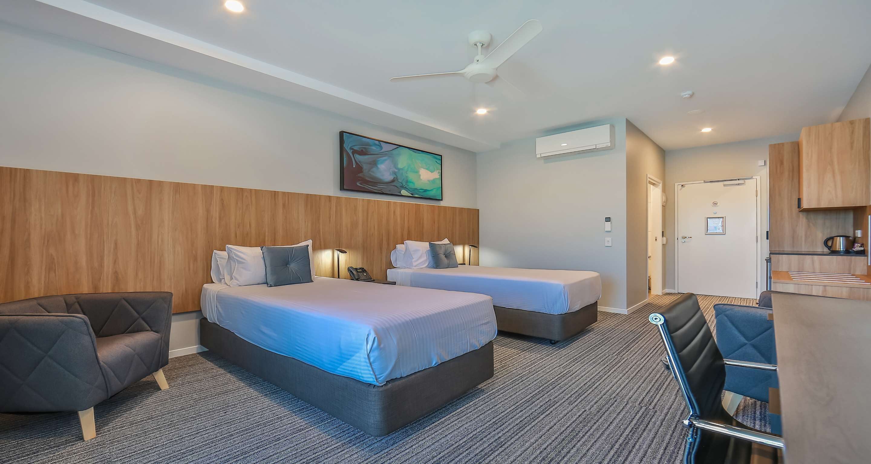 Habitación de hotel con dos camas, un escritorio, una silla, ventilador de techo y aire acondicionado.