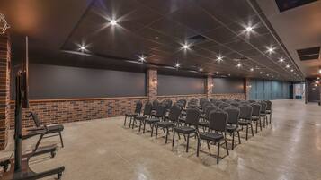 A conference room with rows of chairs, a brick accent wall, and a ceiling with recessed lighting.