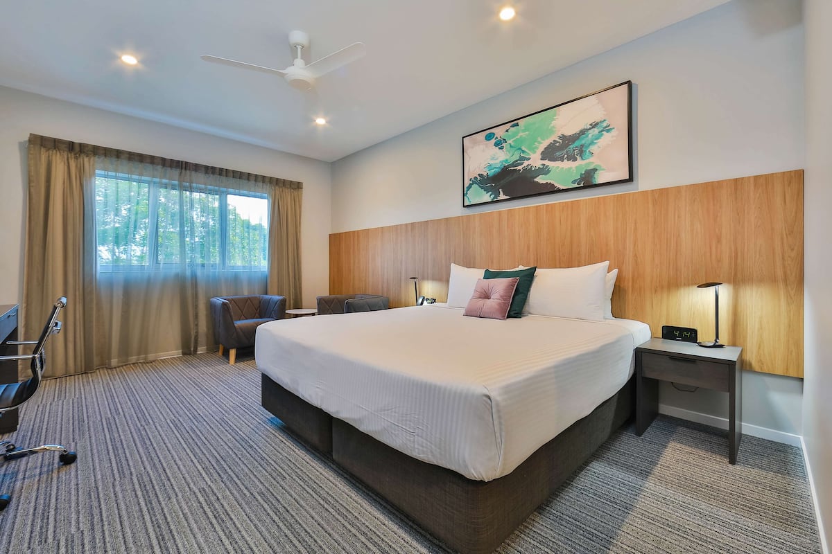 Une chambre d’hôtel avec un grand lit, un bureau, une chaise, une lampe de bureau et un ventilateur de plafond.