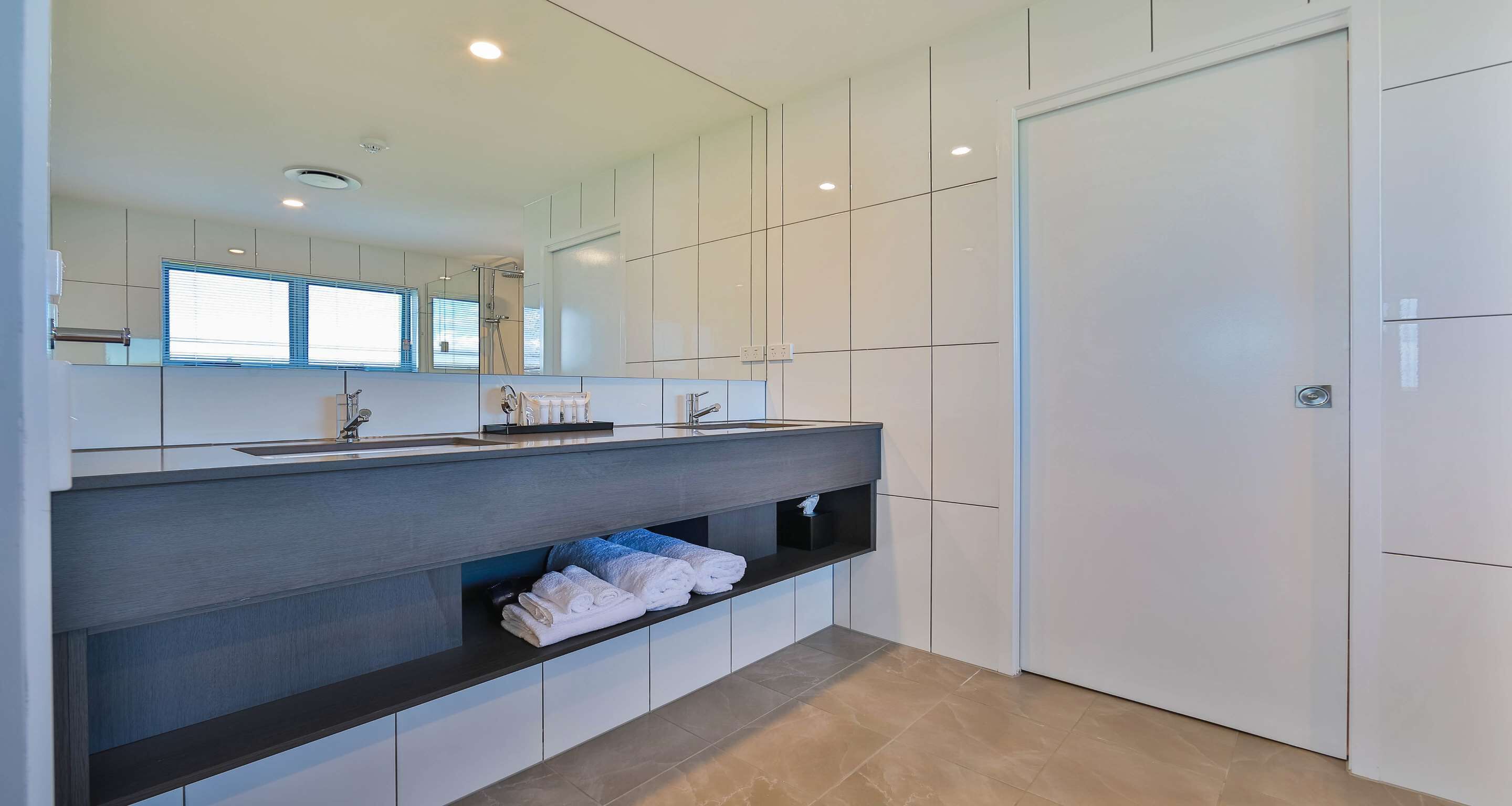 A modern bathroom with a large mirror, white cabinets, a dark countertop, and a towel rack.
