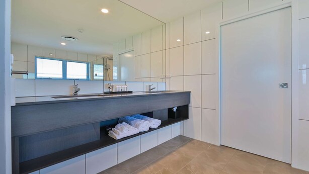 Une salle de bain moderne avec un grand miroir, des meubles blancs, un plan de travail foncé et un porte-serviettes.