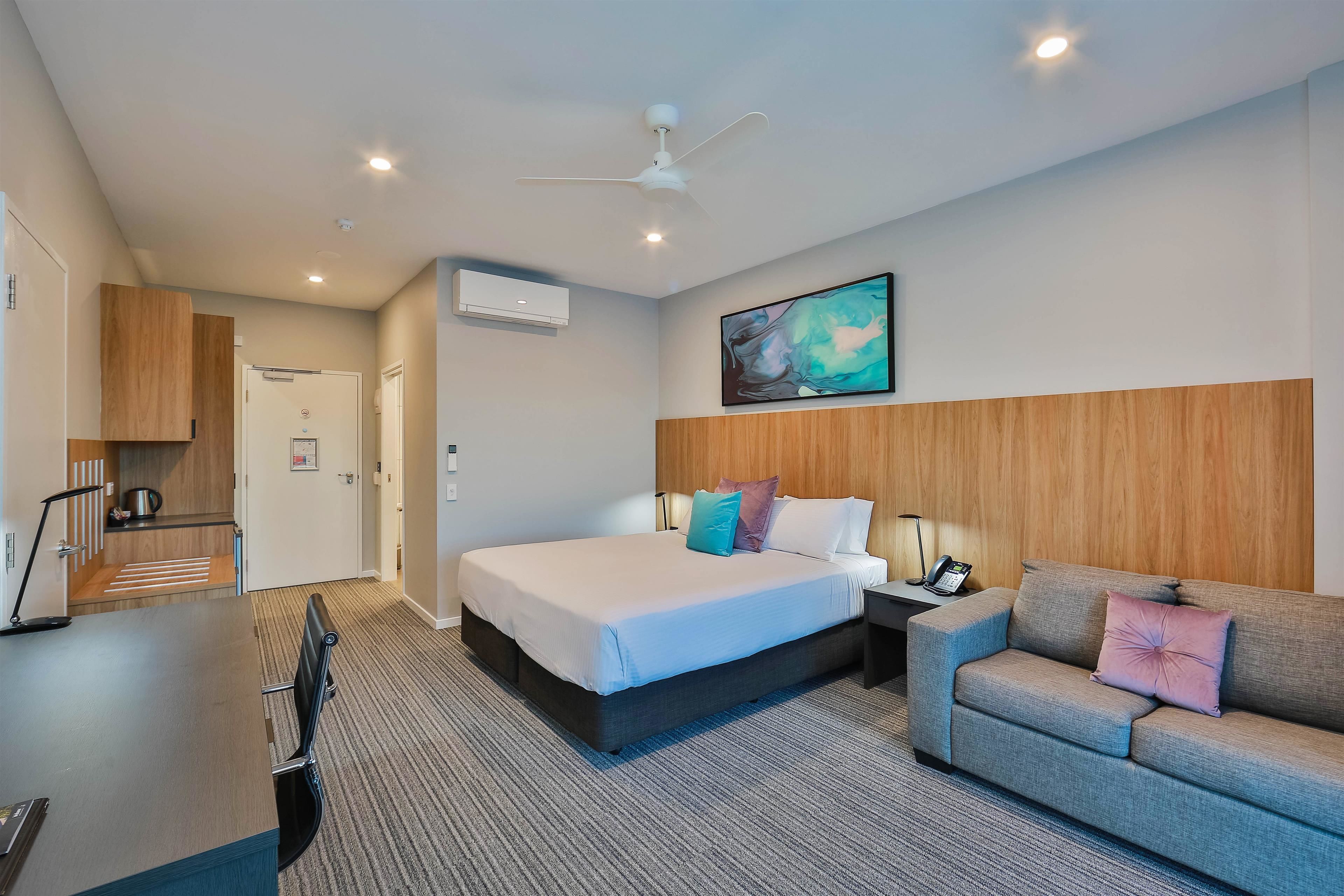 Una habitación de hotel moderna con cama, sofá, escritorio y ventilador de techo.