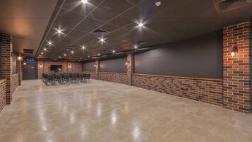 A spacious, well-lit room with a polished concrete floor, brick accents, and a row of chairs facing a dark wall with a mounted screen.